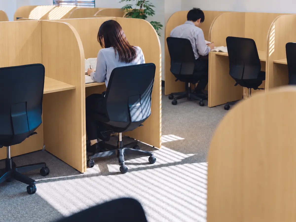 仕切り付きの机で参考書を使って勉強する利用者